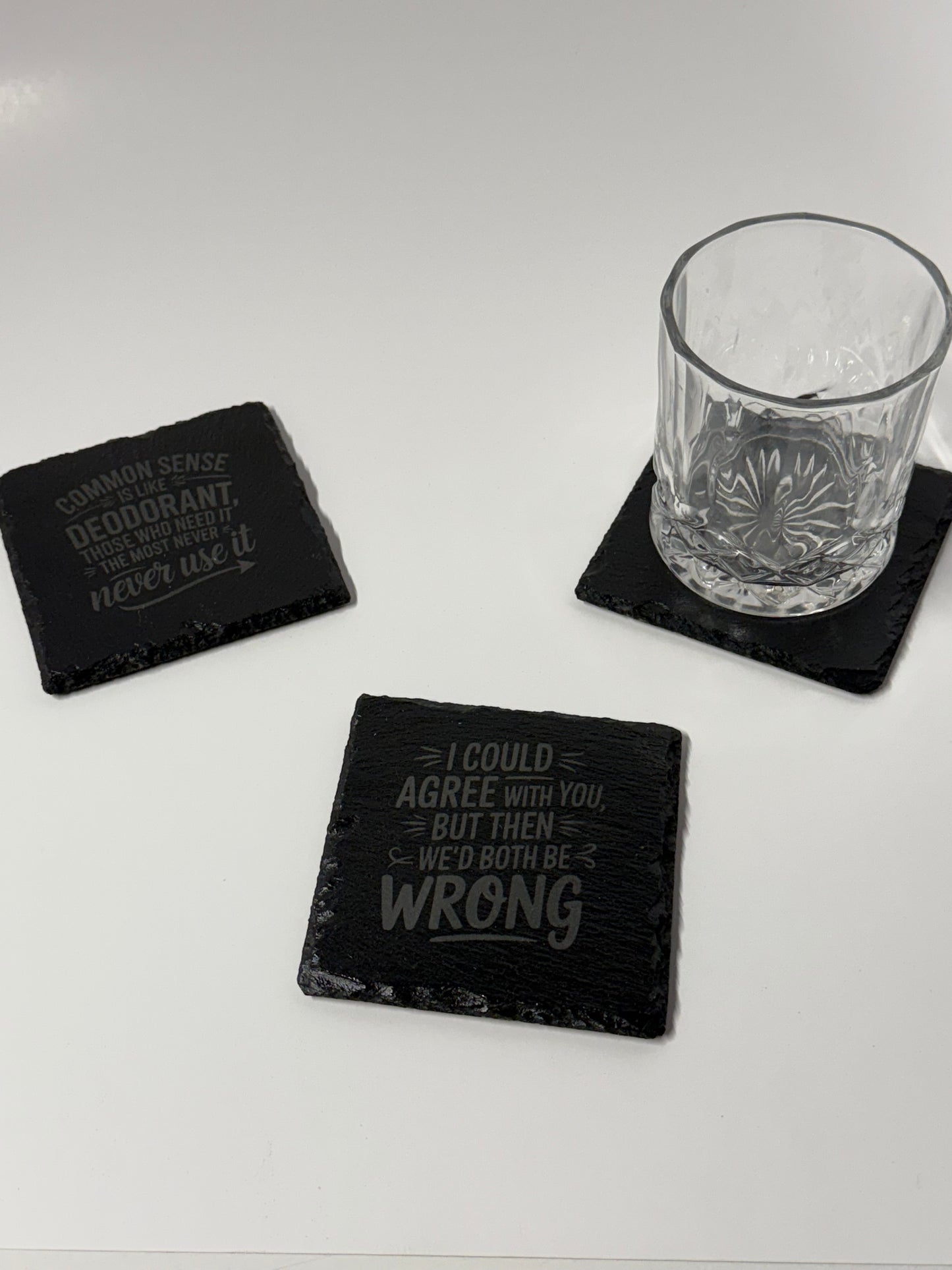 Black coasters with text on a white surface with a glass.
